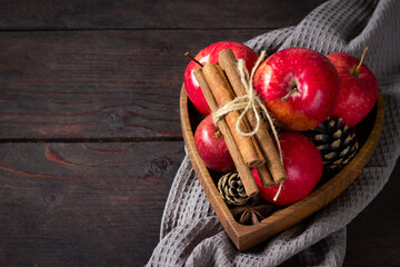 Red ripe apples, cinnamons sticks, pine cones on wooden plate,  brown background. Autumn harvest, autumn template from Thanksgiving