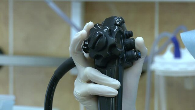 A male hand in medical glove holds an endoscope. Doctor doing ERCP and laparoscopic cholecystectomy inside modern operating room. Surgeon using advance endoscopy technique in gallbladder stone patient