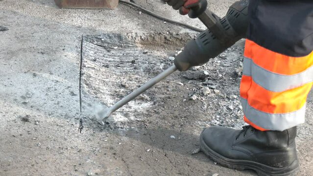 A road worker on a clear day repairs the carriageway of a section of road with a jackhammer.  A worker repairs the road surface with a jackhammer on a summer day. Construction works on the road