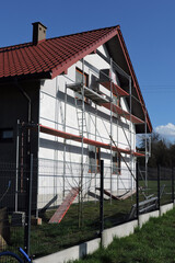 A scaffolding near a wall which is covered with prime before rendering exterior walls, windows and windowsills covered with a protective film