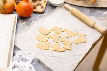 Halloween cookies on a bug, wooden rolling pin. kitchen. Cookies in the form of a ghost, a witch's hat, a pumpkin and a bat on parchment paper.