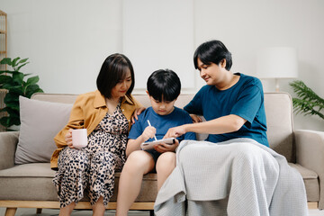 Asian parents and kids laugh use devices together sit on sofa, tech addicted family with children hold laptop phone digital tablet having fun at home