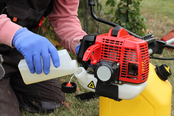 A man in yellow gloves starts up a red trimmer to cut the lawn in autumn
