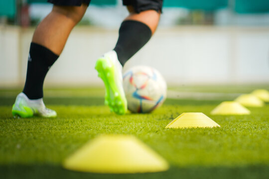 Selective focus at obstacle cones which are placed on turf pitch ground with blurred of a football player is dribbling the ball for training. Sport training in action and backgorund photo.
