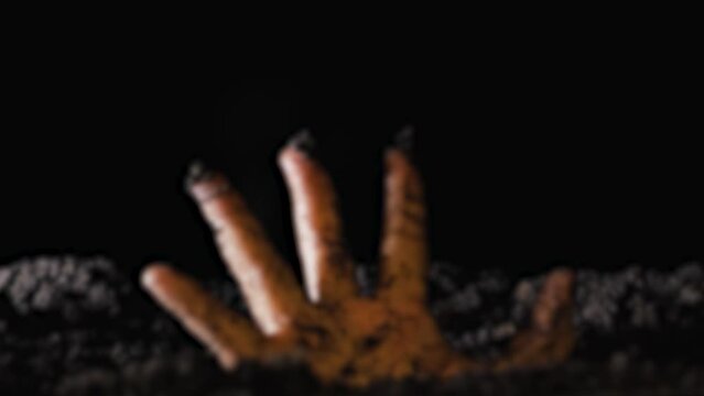 A close-up of a dead man's hand climbing out of the ground. A zombie hand rises from the grave at night. Rise of the dead. Blurred video