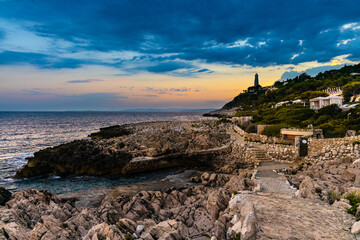 Fototapeta premium Sunset over rocky coast of Cap Ferrat cape with Phare Lighthouse near Saint-Jean-Cap-Ferrat resort town and Nice at French Riviera in France