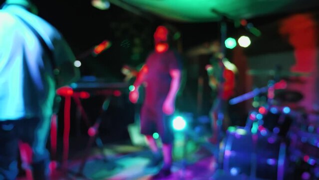 A reggae band performing on stage. Blurred video. Band members playing and dancing. View from the stage. On the stage bright flashes of light show