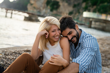 Romantic couple sitting at the beach. Attractive woman and handsome man spending the evening together and laughing while enjoying summer vacation.