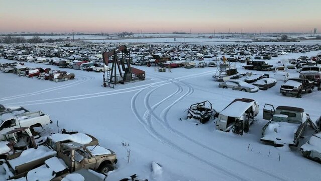 Abandoned junkyard of cars covered in snow winter morning. Drone footage flying low over scrap yard of old cars. 