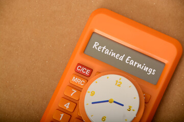 Paper clock and calculator with text RETAINED EARNINGS.also known as accumulated earnings or retained profits