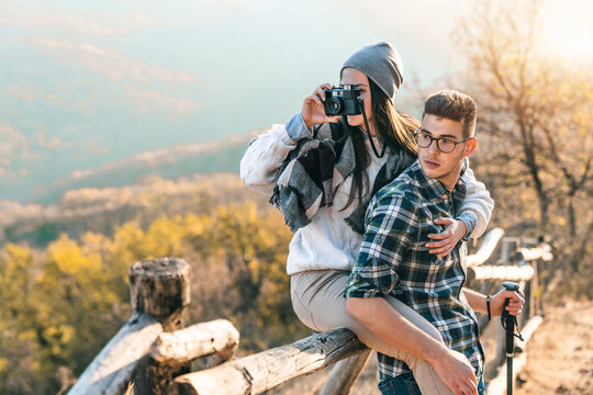 Photo of a young couple feeling close and taking photos of nature during the hike. They are watching curiously into the distance.