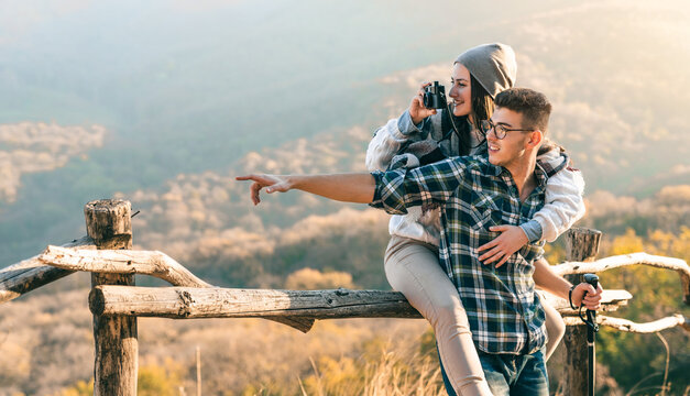 Joyful woman, can’t hide her delight of the majestic nature, during her hike with a boyfriend. Couple taking photos outdoors, pointing at the view.