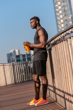 Full length of young African athlete in sportswear holding water bottle while resting after training outdoors
