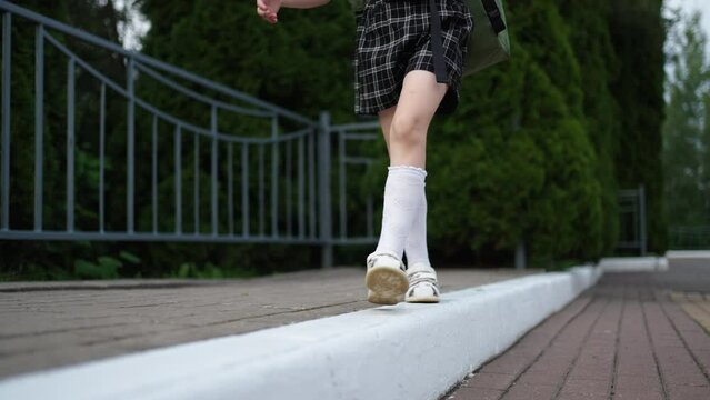 First Grader Girl Walking Over Curb In Park, Closeup View Of Child Legs, Schoolgirl After Classes