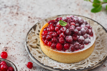 Tartlet with fresh cowberry, cream and sugar powder on rustic background. Berry tart