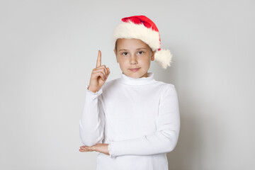 Cute Christmas kid little girl wearing red Santa hat pointing up on white background