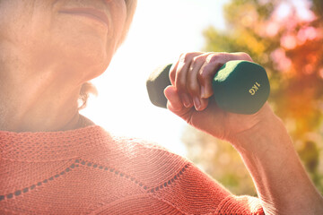Senior woman doing physical exercise outdoors with dumbbells.  Senior healthcare and sport concept.