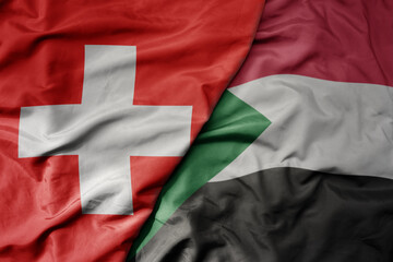 big waving national colorful flag of switzerland and national flag of sudan .