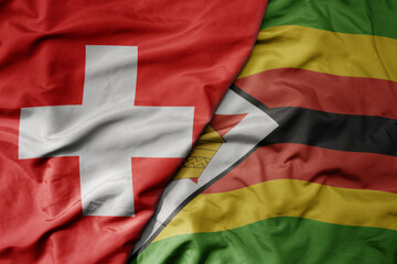 big waving national colorful flag of switzerland and national flag of zimbabwe .