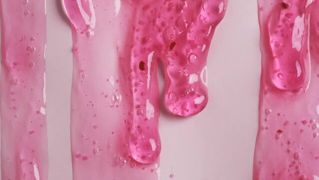 Liquid drops of transparent pink cosmetic sample texture with bubbles  flowing on the pink surface. Macro shot of peeling gel with raspberry dripping on the wall. Rose shower gel