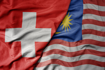 Fototapeta premium big waving national colorful flag of switzerland and national flag of malaysia .