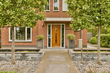 a red brick house with trees in the front and walkway leading up to the front door, on a sunny day