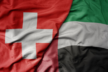 big waving national colorful flag of switzerland and national flag of united arab emirates .