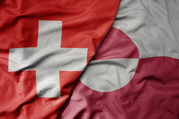 big waving national colorful flag of switzerland and national flag of greenland .