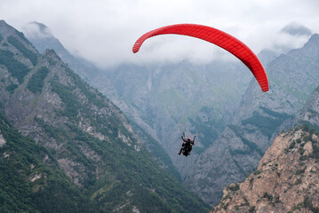 red paraglider flies against the background of mountains and clouds, rear view