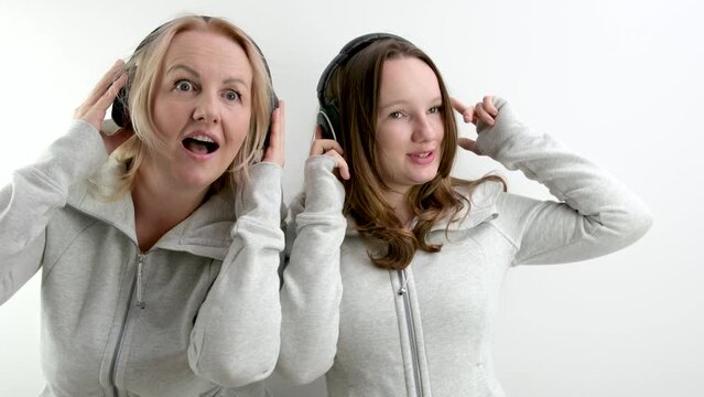 mother and daughter in headphones make eyes, smile, take pictures, family photo session on a white background, identical clothes, beautiful people, women, teenager and adult woman, expression