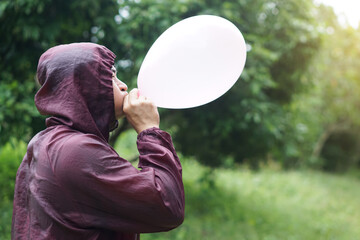 Asian man is blowing, inflating air into a balloon in the park. Concept, prepare balloon for playing games as a toy, decorate party or celebration. Recreation or leisure activity. Fun and happy time. 