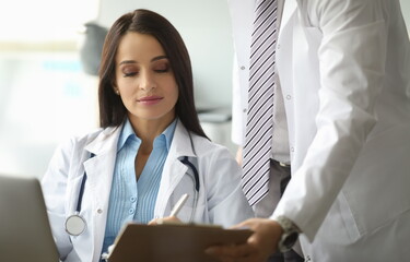 Portrait of woman in medical gown signing important documents. Man holding paper folder. Family therapist in clinic office. Healthcare and treatment concept