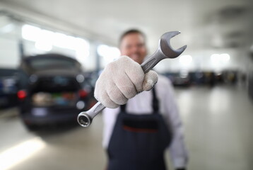 Focus on automechanic male hand holding important tool and showing utility for fixing car at camera. Machinery checkup and service station concept. Blurred background