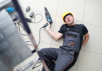 Occupational Safety and Health concept. Male worker with power tool in his hands fell down stairs to floor. Lies and writhes in pain. Intentional harm health