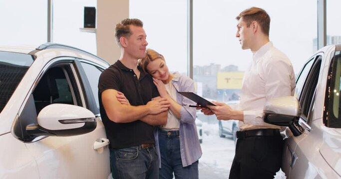 conversation with a specialist, dealer giving instructions, recommendation to happy family customers. slow motion. Happy couple talking with manager while buying car at dealership center.