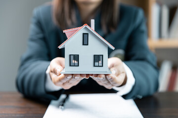 Small toy house in hands, close up of female hands sheltering modern house, get insurance or loan real estate or property. Approved mortgage application form, concerning mortgage loan offer.