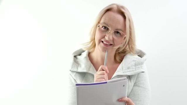 European woman with glasses bites pen writes on sheet of paper document comes up with story writer magazine design meditate look to side think blond hair in studio white background. author of book