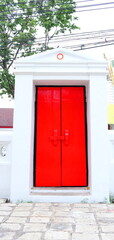 Bright red painted closed wood door and white painted cement frame of door in temple, Thailand.