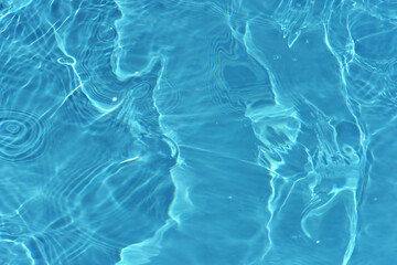 Blue water with ripples on the surface. Defocus blurred transparent blue colored clear calm water surface texture with splashes and bubbles. Water waves with shining pattern texture background.
