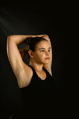 young woman stretching wearing a black tshirt on a black background , fitness and yoga