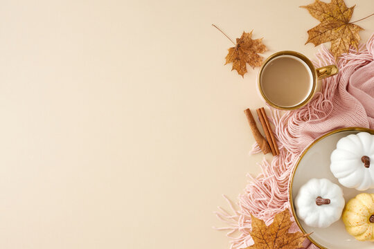 Experience the warmth of home during autumn. Top view photo of cozy cute pleid, hot coffee, pumpkins on the plate, cinnamon sticks, dry autumn leaves on pastel beige background with ad zone