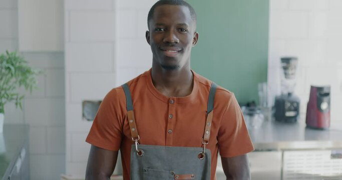 Slow motion portrait of attractive African American man professional barista standing in modern coffee house wearing apron smiling looking at camera