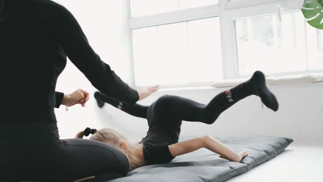 Little laughing gymnastic girl doing stretching exercise with help of her trainer