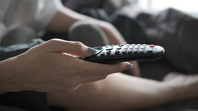 Woman hand selects internet tv channels with remote control. Close up view. on her bed in the morning weekend.