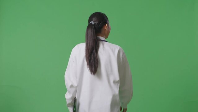 Back View Of Asian Female Doctor With Stethoscope Holding A Tablet While Walking On Green Screen Background In The Hospital
