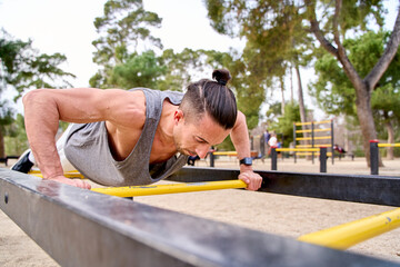 man training in a park doing push-ups on a calisthenics bar