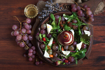 Bright and tasty salad with brie cheese, red pear, grapes, arugula, nuts and dried fruits on a brown plate on a wooden background