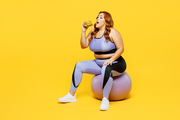 Full body side view young chubby plus size big fat fit woman wearing blue top warm up training sit on fit ball drink water isolated on plain yellow background studio home gym. Workout sport concept. - Powered by Adobe