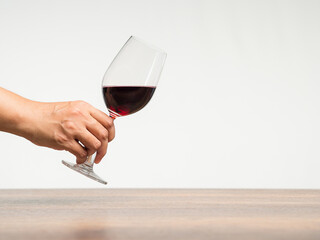 Hand holding a glass of red wine against a gray background.