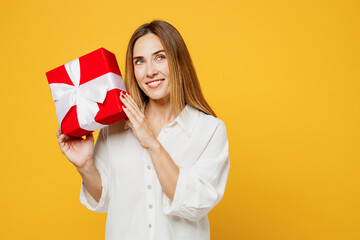 Fototapeta premium Young smiling cheerful caucasian happy woman wears white shirt casual clothes hold present box with gift ribbon bow look aside isolated on plain yellow background studio portrait. Lifestyle concept.
